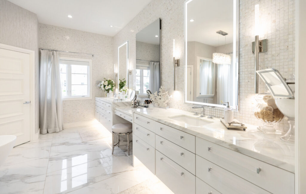 Luxury white master bathroom with dual vanity, lighted mirrors, white marble countertops, and patterned tile walls.