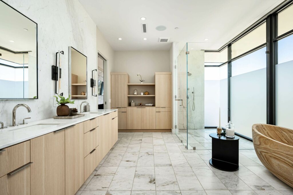 Luxurious master bathroom by Woodcrest Design with dual vanity, light wood cabinetry, shower, and wooden tub.