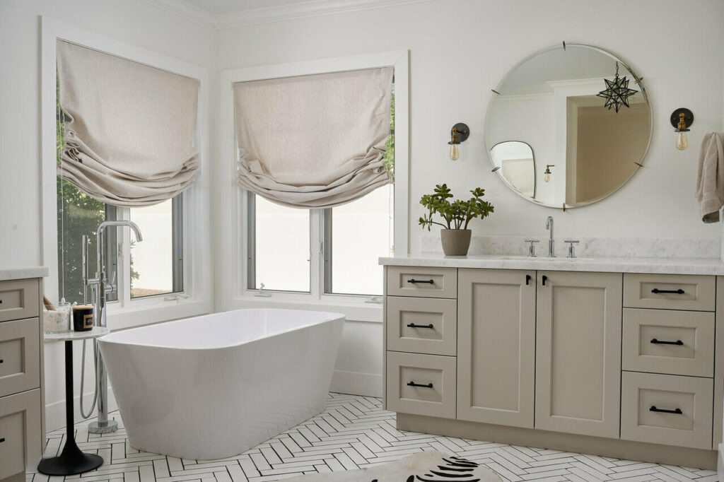 Luxurious master bathroom by Woodcrest Design with freestanding tub, Roman shades, herringbone tile, and vanity.