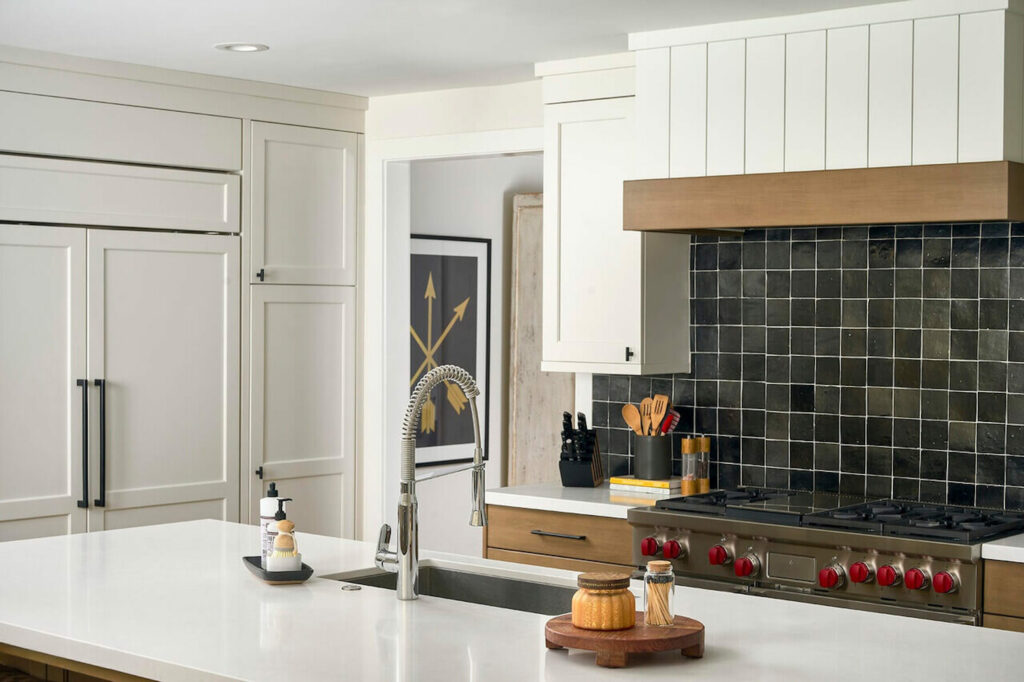 Modern kitchen with white shaker cabinets, black square tile backsplash, stainless steel range, and large island.