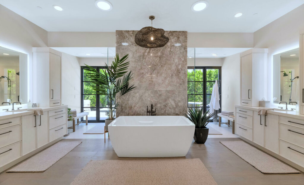 Luxurious master bathroom by Woodcrest Design, featuring a freestanding bathtub, dual vanities, modern cabinetry, large windows, and a textured accent wall.