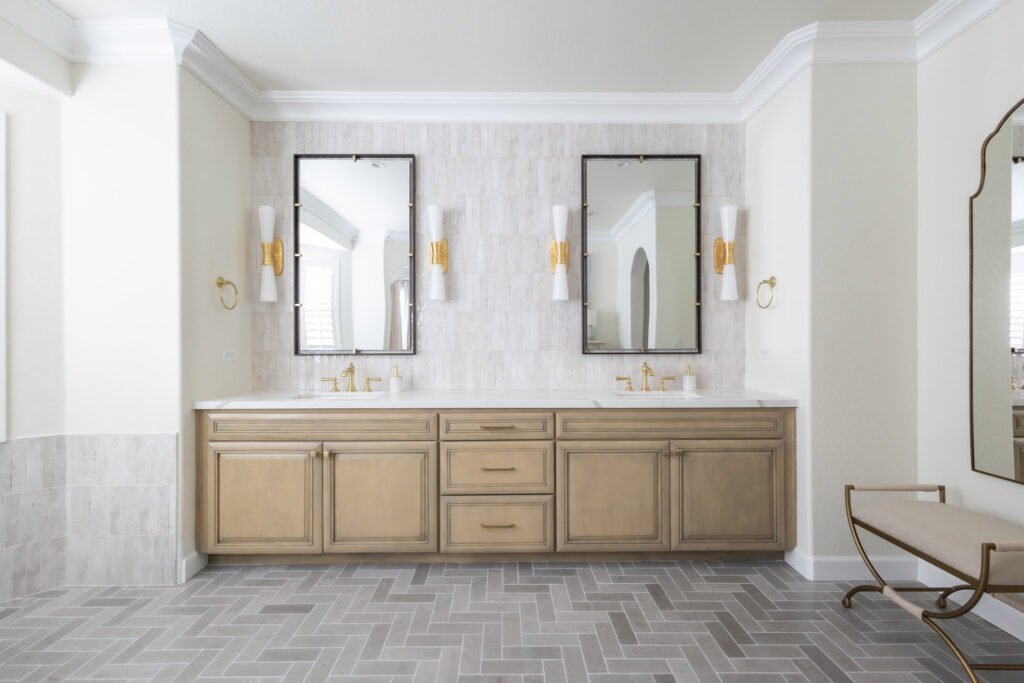 Luxury bathroom with twin vanities, gold fixtures, black-framed mirrors, and white wall sconces. Herringbone tile floor.