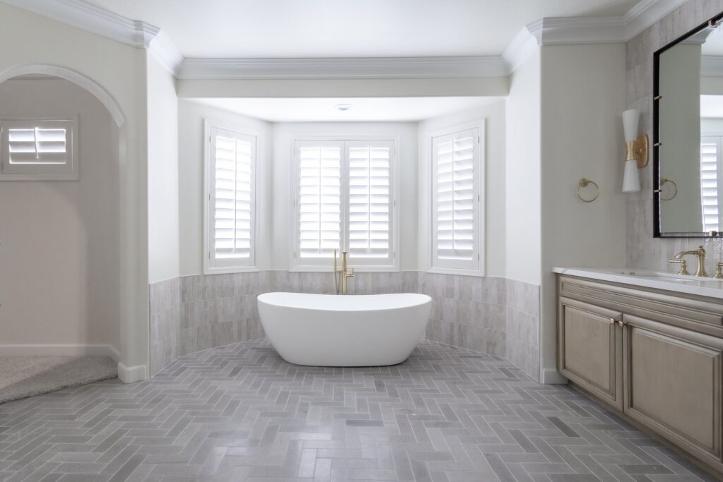 Luxurious bathroom with a freestanding tub under bay windows, herringbone tile floor, and sophisticated vanity by Woodcrest Design.