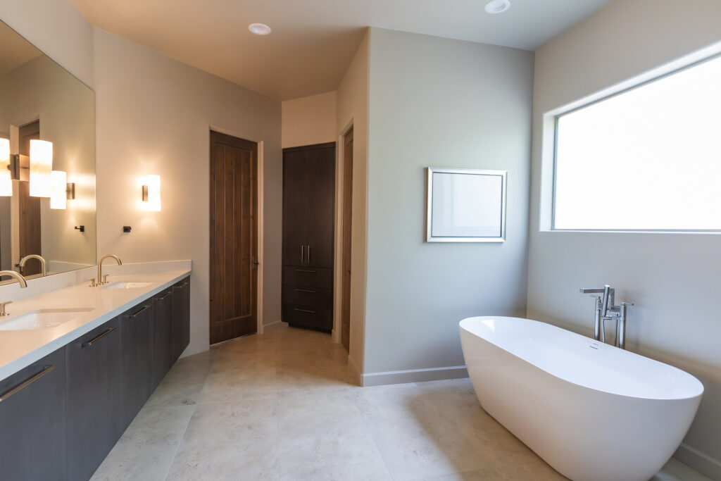 Luxurious beige bathroom with dual sinks, modern vanity, freestanding tub, and dark wood cabinetry by Woodcrest Design.